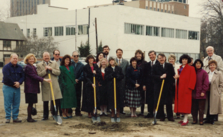 Diane standing with shovel and group of people in dirt lot in the 1990's.