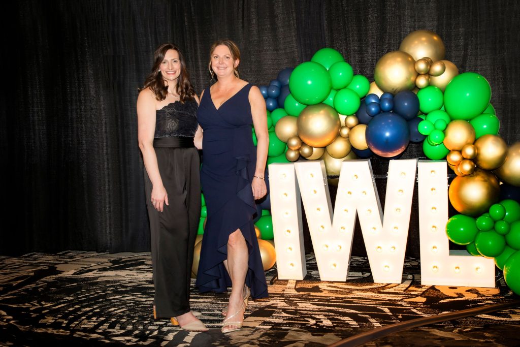 two women in fancy dresses in front of IWL letters and balloons