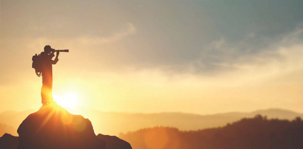 man on mountaintop looking out with telescope