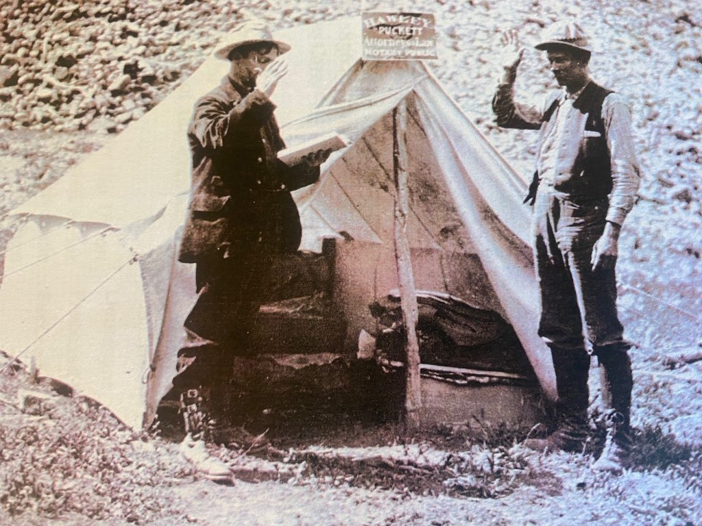 Two men in 19th century taking an oath in front of a tent.