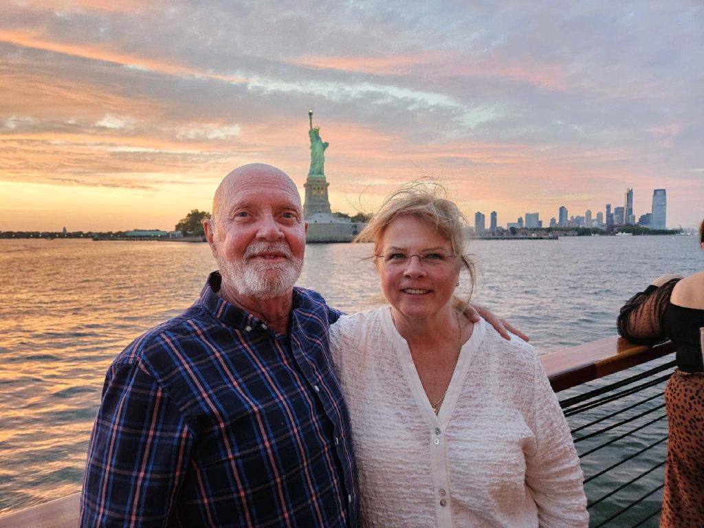 two adults smiling outside the statue of liberty