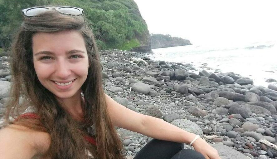 woman smiling, sitting on rocks at the ocean