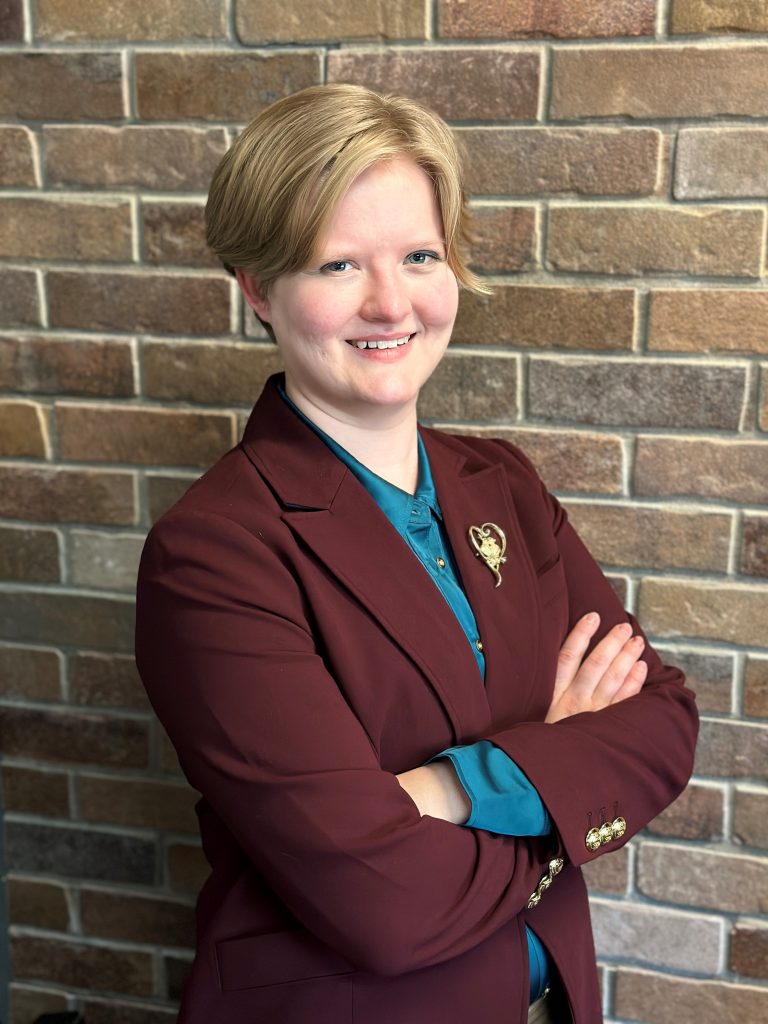 Woman crossing arms and smiling in front of brick wall